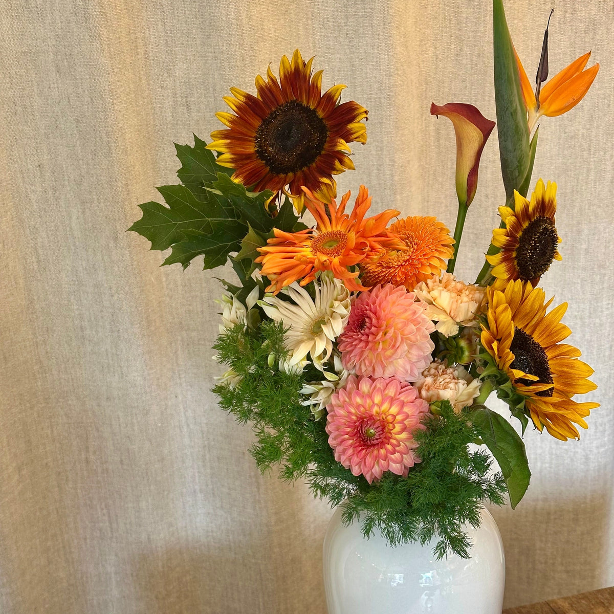 Le Solaire, tournesols, dahlias roses, gerberas orange et strelitzia en vase blanc - Bouquetier Paris 17