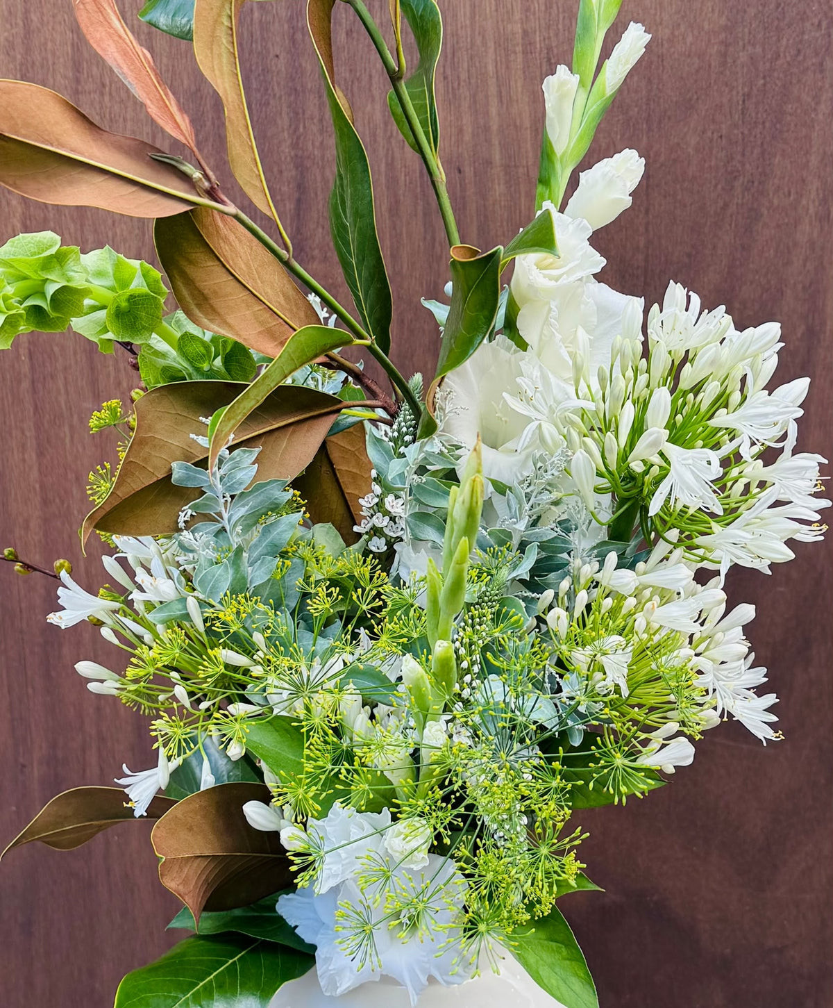 Le Végétal - agapanthes et glaïeuls blancs, feuillage de magnolia cuivré, fond bois - Bouquetier Paris 17
