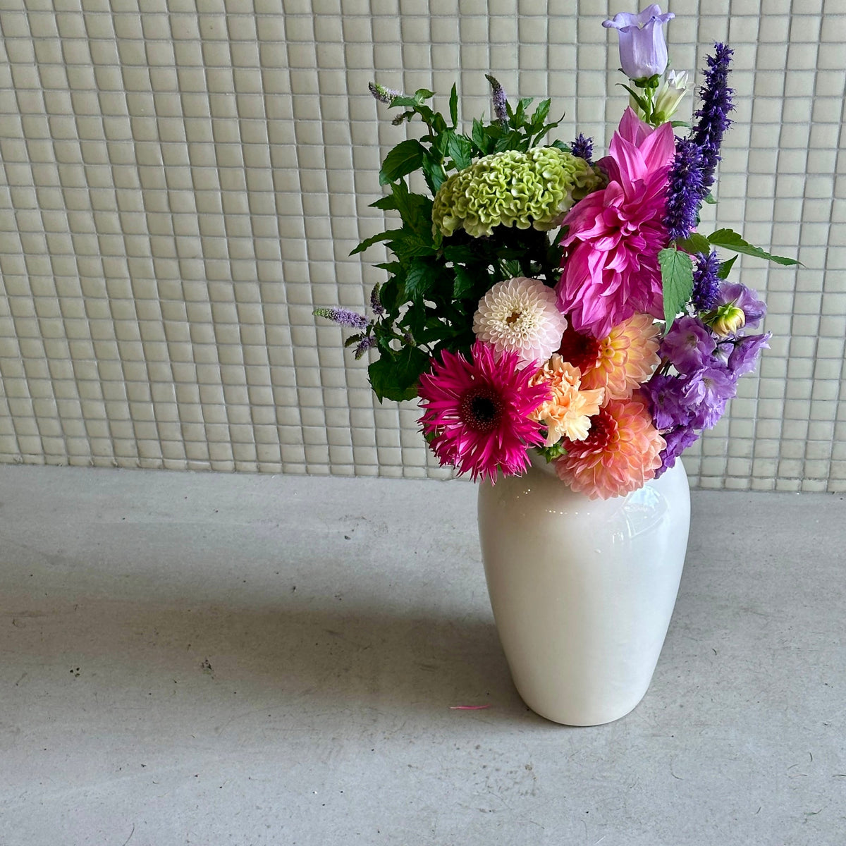 Le Coloré, dahlias fuchsia et pêche, célosie verte et delphinium mauve en vase blanc - Bouquetier Paris 17