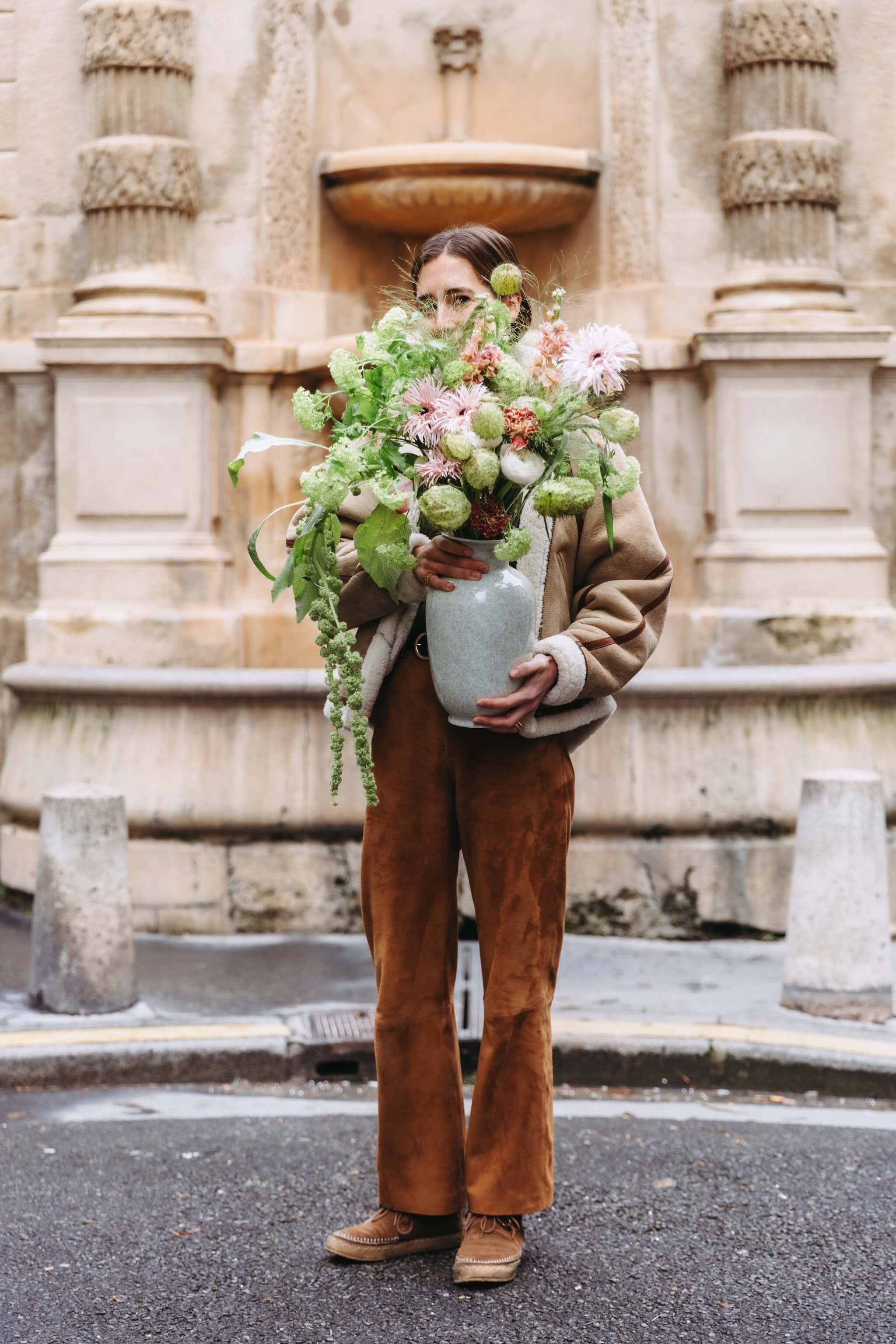 Fleuriste tenant une composition de fleurs de saison dans un vase, en extérieur