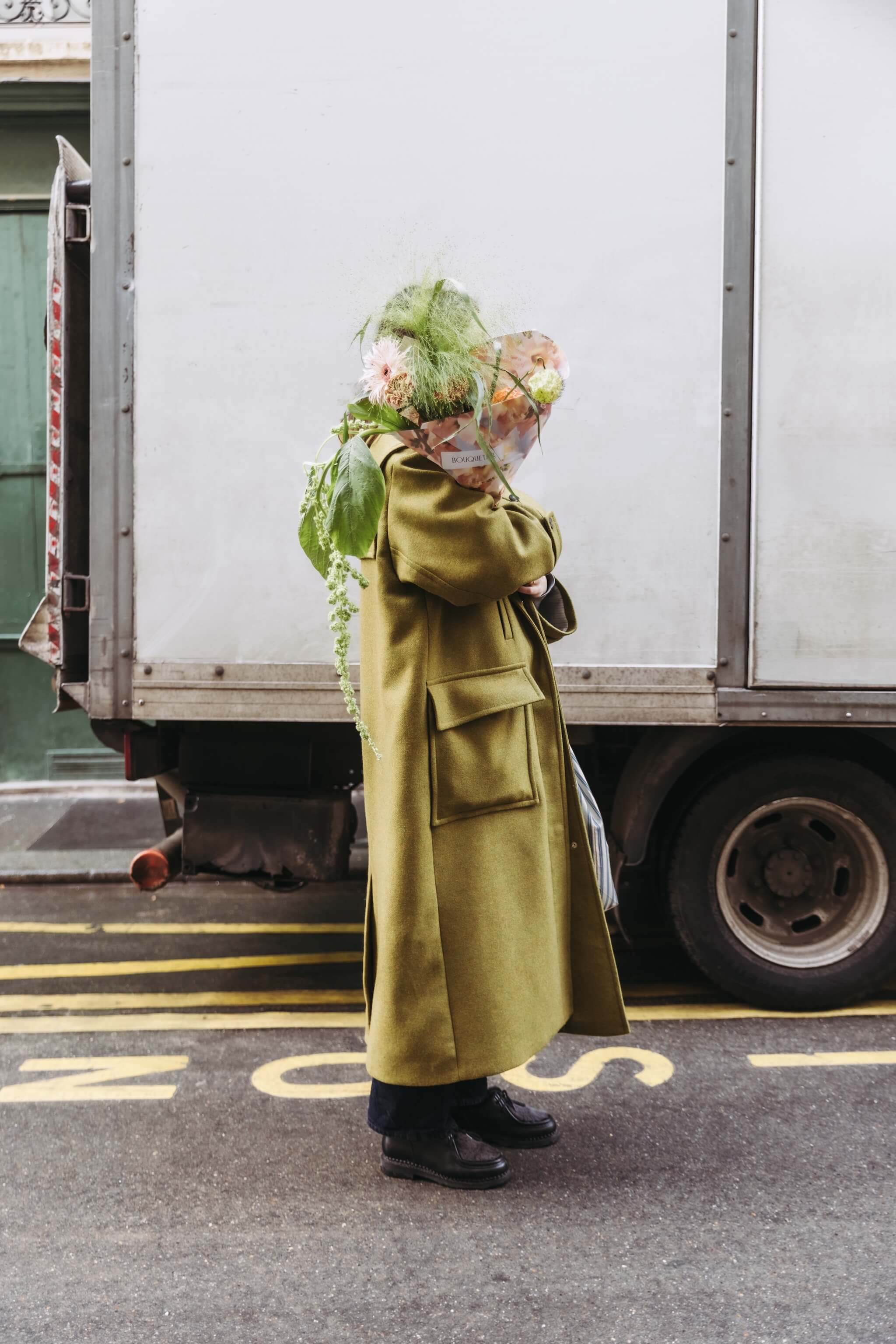 Personne portant un bouquet de fleurs de saison et un sac de courses dans la rue, en contexte urbain