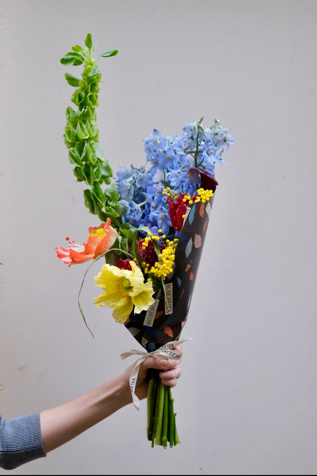 Bouquet de fleurs de saison emballé dans le papier Bouquetier, tenu à la main