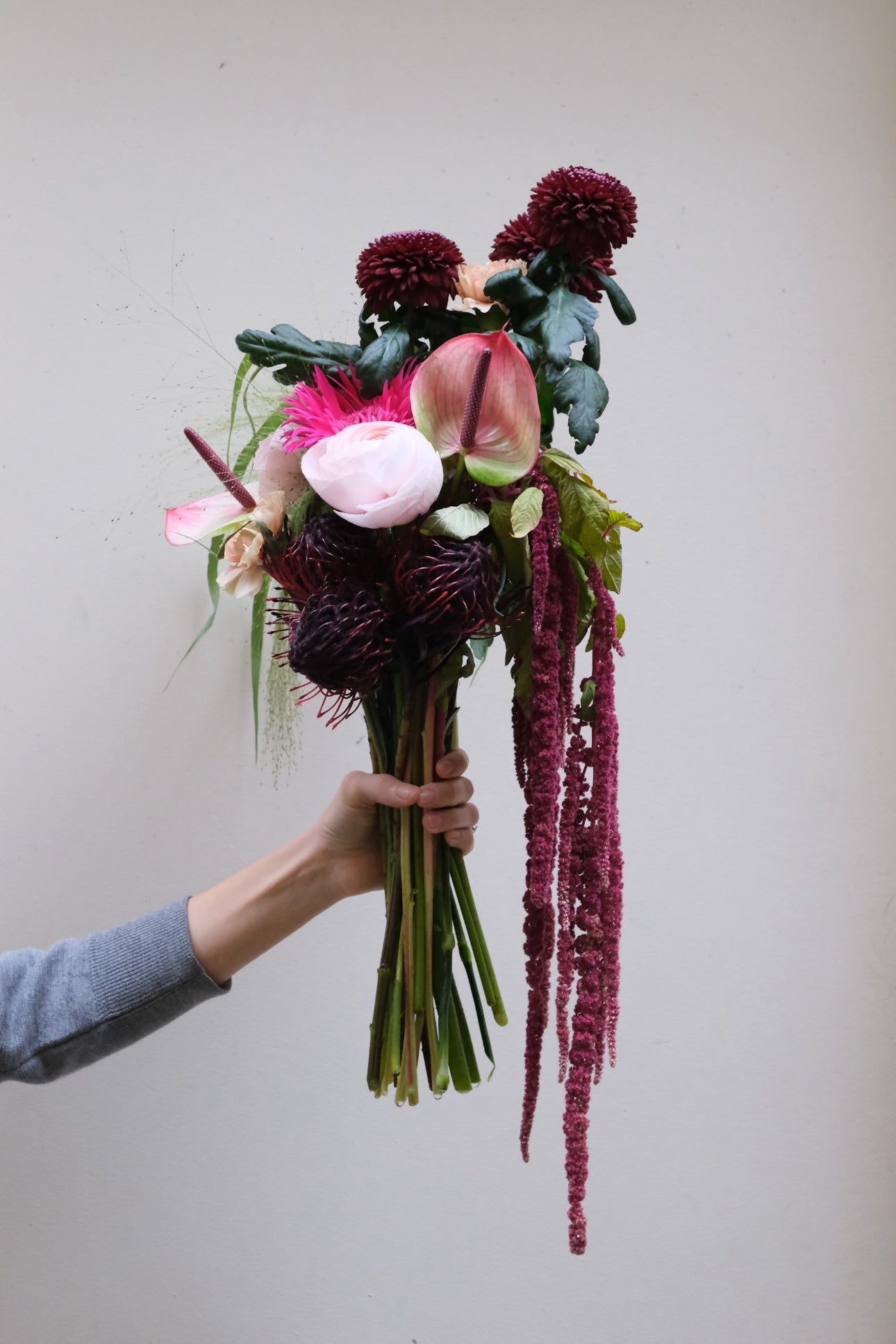 Bouquet de fleurs de saison aux tons roses et bordeaux, tenu à la main
