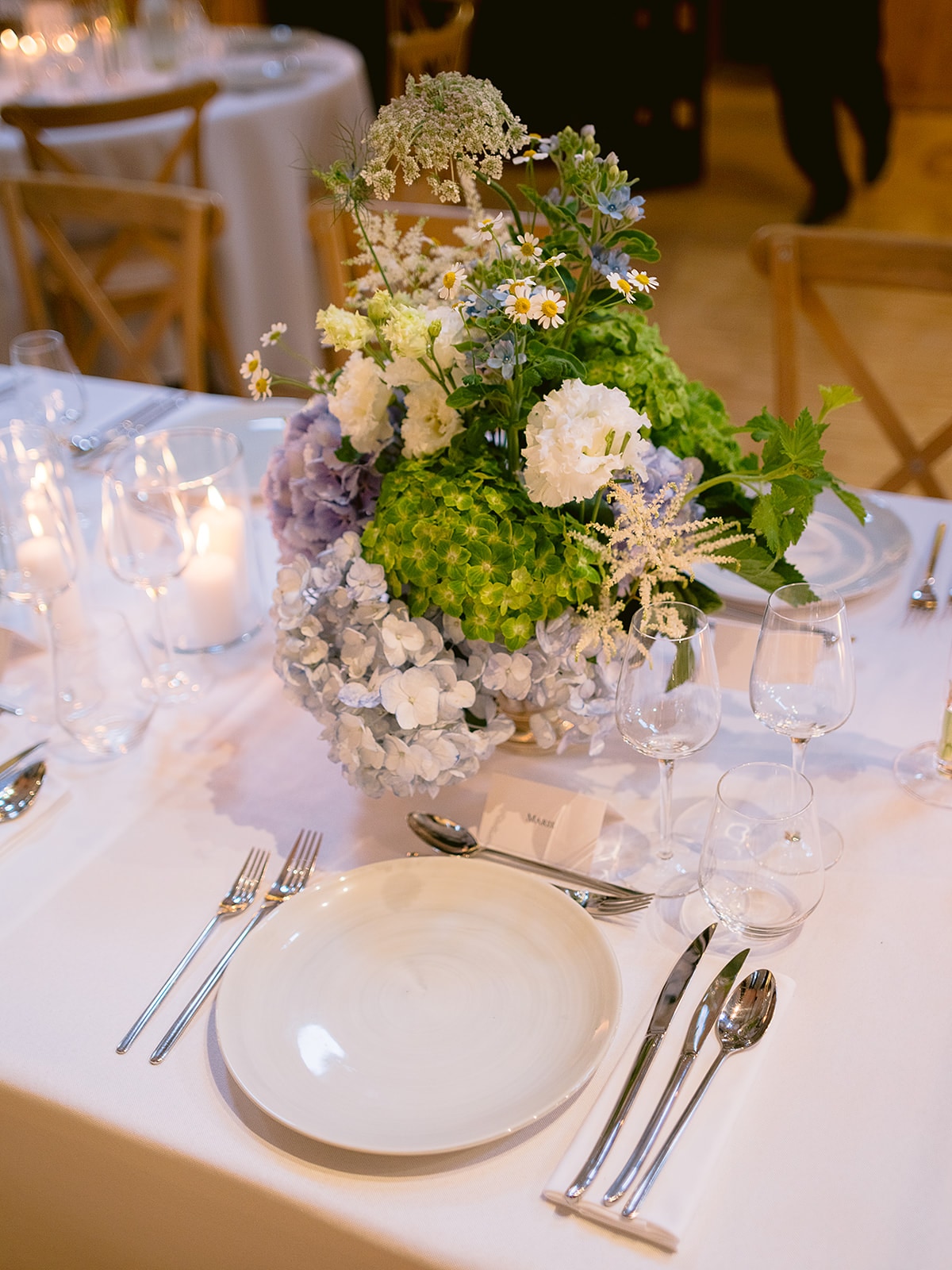 Centre de table de mariage en fleurs vertes et blanches avec bougies sur une nappe blanche - Bouquetier Paris 17