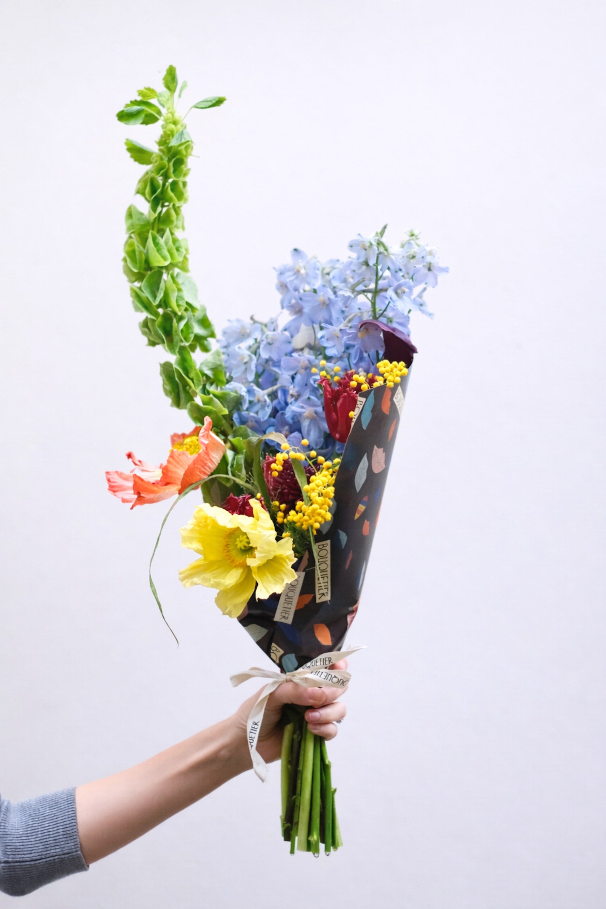 Bouquet de fleurs de saison emballé dans le papier Bouquetier, tenu à la main